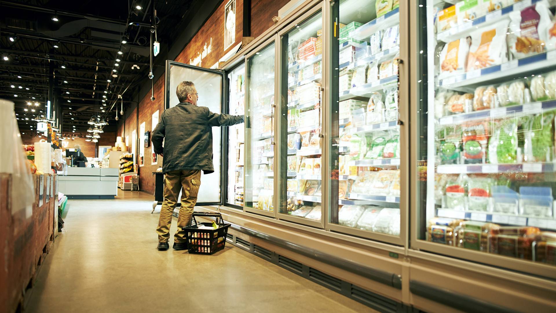 a male shopper picking something out of a commercial freezer