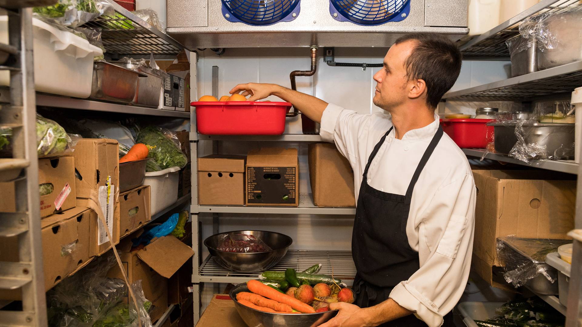 a man in an industrial refrigerator picking out vegetables